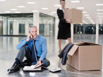 Two people moving boxes into an office