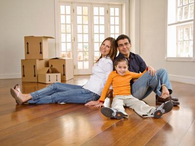 Smiling family sits on floor of empty house with moving boxes in background